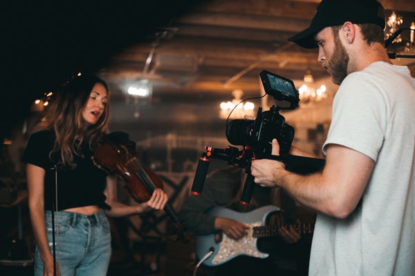 man filming a woman playing violin